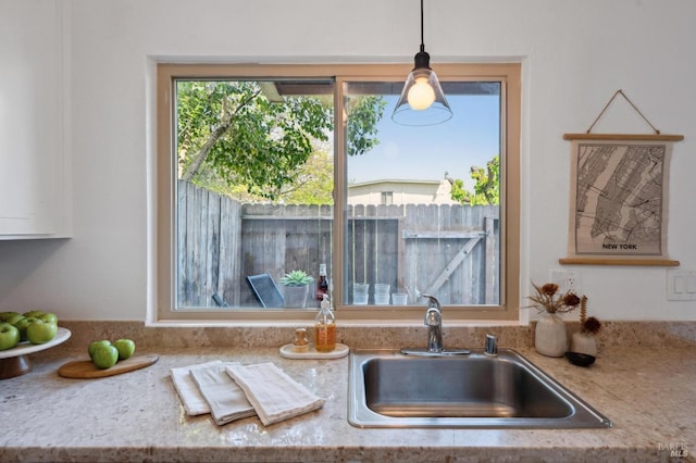 kitchen featuring decorative light fixtures, light stone counters, and a sink