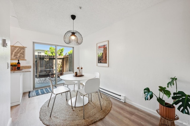 dining area featuring a textured ceiling, baseboards, baseboard heating, and light wood-style flooring