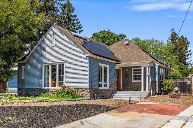 bungalow featuring covered porch, roof with shingles, solar panels, and stone siding
