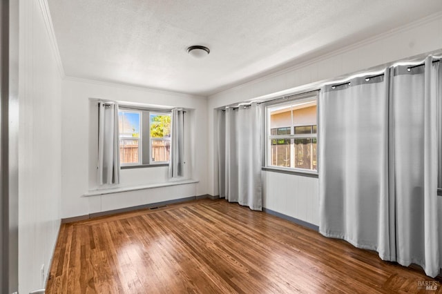 empty room with visible vents, ornamental molding, a textured ceiling, and wood finished floors