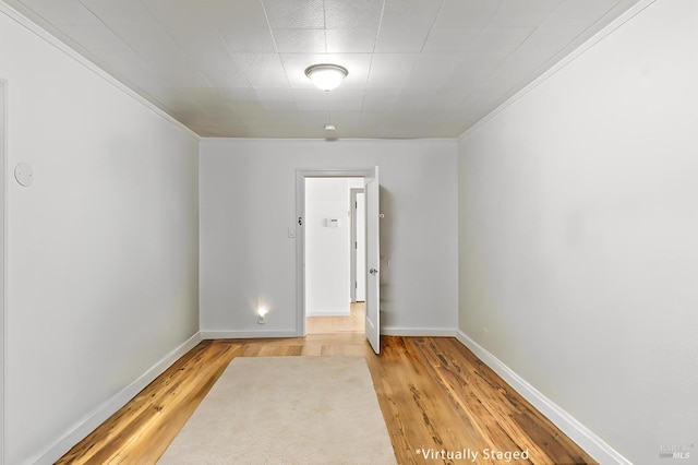 spare room with crown molding, light wood finished floors, and baseboards