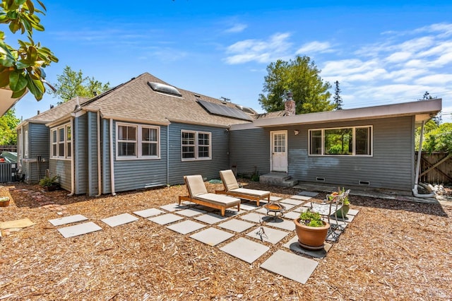 back of property with fence, a patio, a shingled roof, entry steps, and solar panels