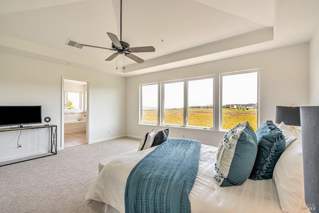 carpeted bedroom featuring baseboards, multiple windows, a tray ceiling, and connected bathroom