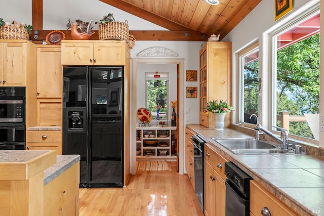 kitchen with a sink, lofted ceiling with beams, black appliances, light brown cabinets, and light wood-style flooring