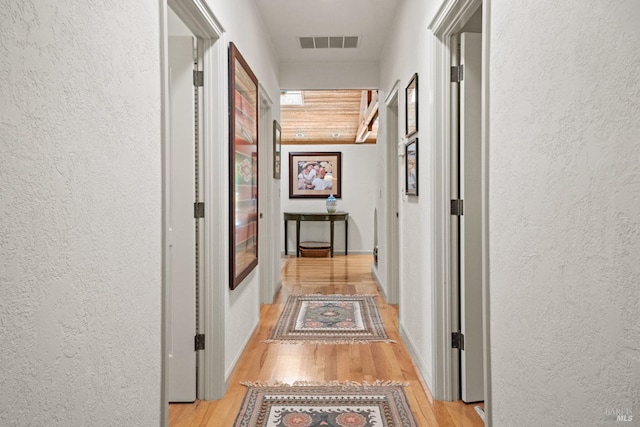hallway with visible vents, a textured wall, and light wood-style floors