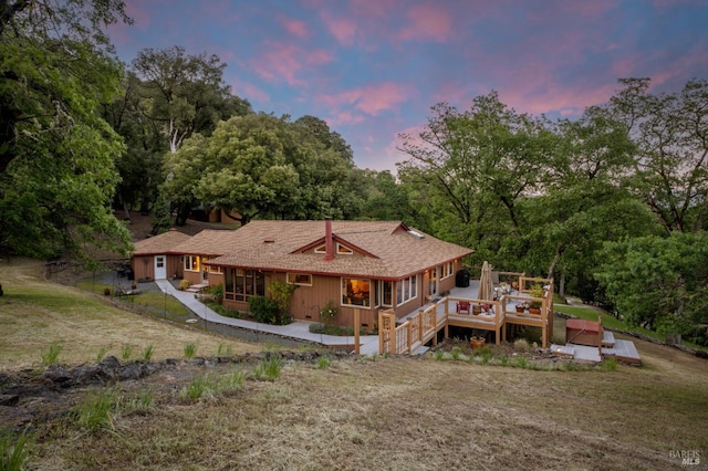 rear view of property featuring a sunroom, a wooden deck, and a yard