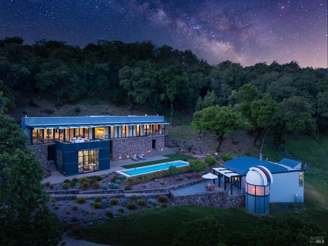 rear view of house with a wooded view, a patio, a hot tub, and an outdoor pool