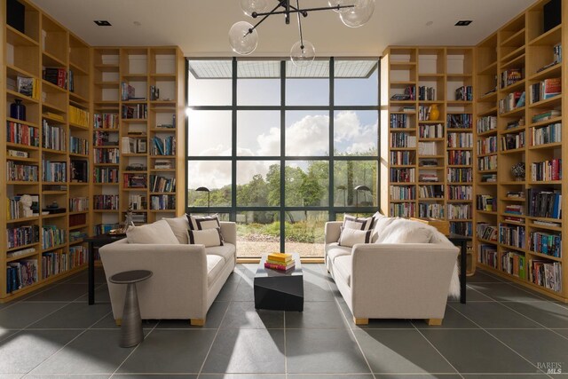 living area with wall of books, dark tile patterned floors, expansive windows, and an inviting chandelier