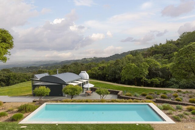 outdoor pool featuring a patio, a yard, and a wooded view