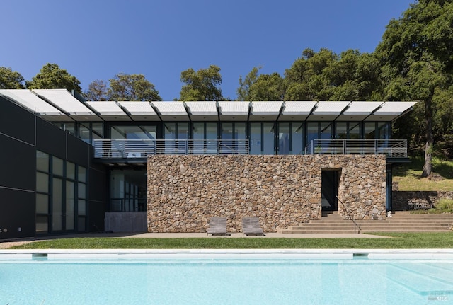 back of house with an outdoor pool and a balcony