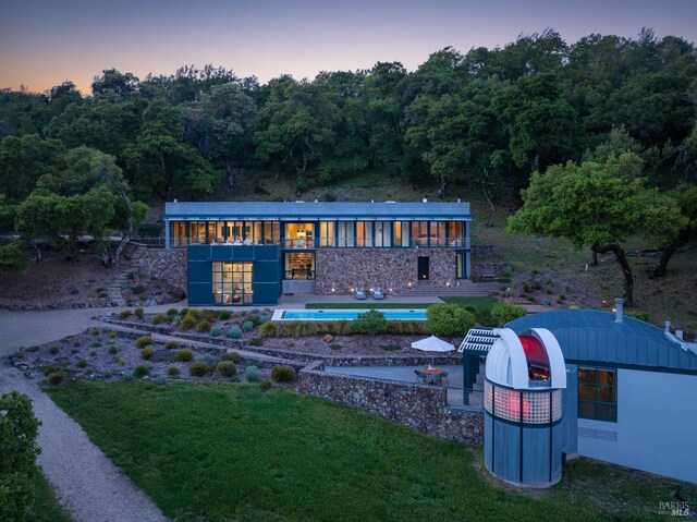 rear view of house with a patio area, a yard, a wooded view, and a pool