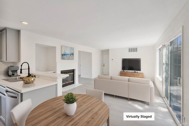 living room featuring a fireplace with flush hearth, light wood finished floors, recessed lighting, and visible vents
