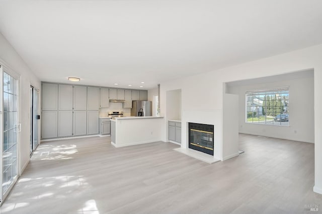 unfurnished living room with a glass covered fireplace, baseboards, and light wood-style flooring