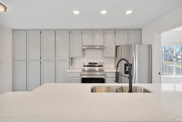 kitchen featuring light stone countertops, a sink, stainless steel appliances, recessed lighting, and under cabinet range hood