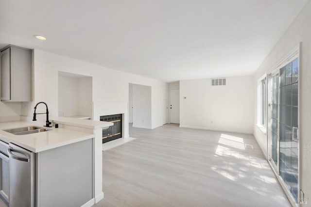 kitchen featuring a sink, dishwasher, light countertops, gray cabinets, and open floor plan
