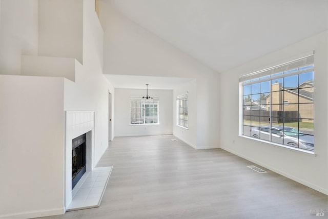 unfurnished living room featuring a notable chandelier, light wood finished floors, a fireplace, high vaulted ceiling, and visible vents