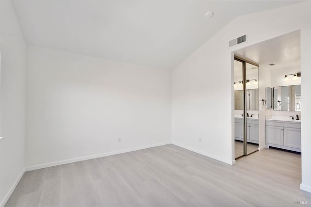 unfurnished bedroom with visible vents, a sink, light wood finished floors, and vaulted ceiling