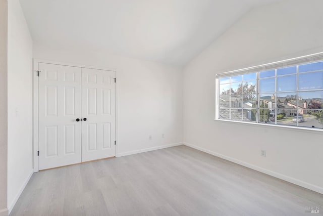 unfurnished bedroom with baseboards, wood finished floors, vaulted ceiling, and a closet