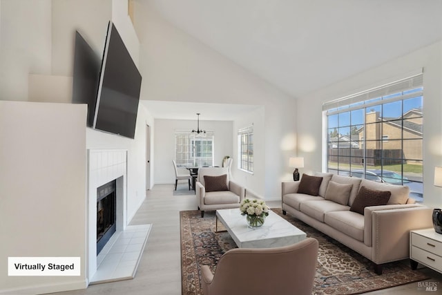 living area featuring high vaulted ceiling, plenty of natural light, light wood-type flooring, and a chandelier