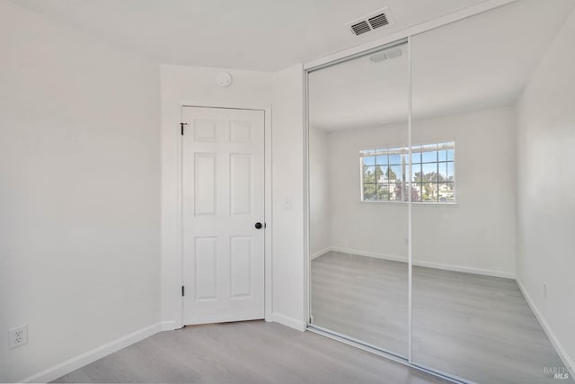 unfurnished bedroom with visible vents, baseboards, wood finished floors, and a closet