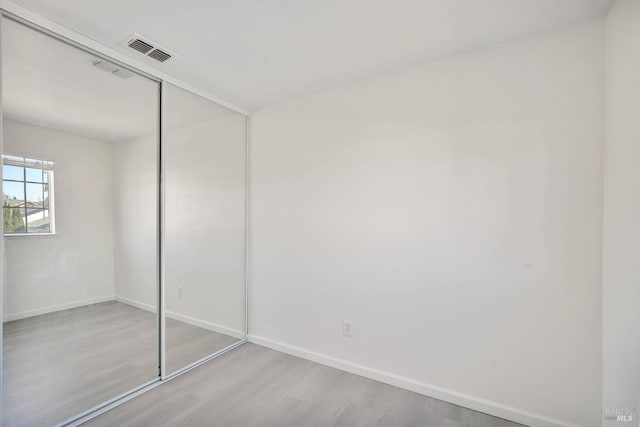 unfurnished bedroom with baseboards, visible vents, wood finished floors, and a closet