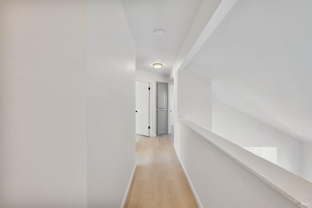 hallway with baseboards, an upstairs landing, and light wood-style flooring