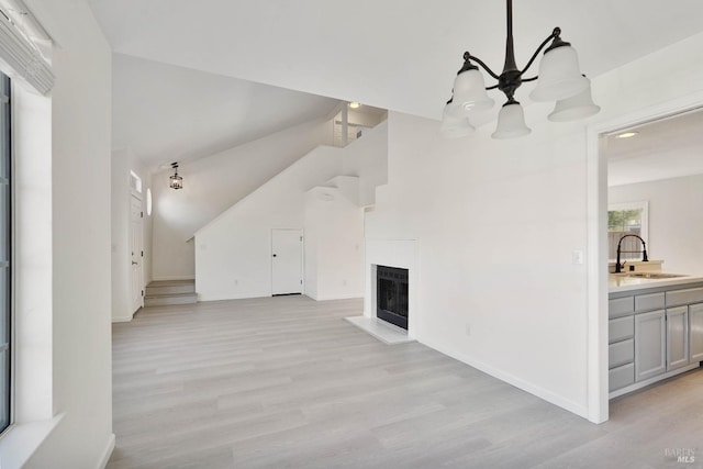 additional living space featuring a fireplace, baseboards, a sink, light wood-style flooring, and vaulted ceiling