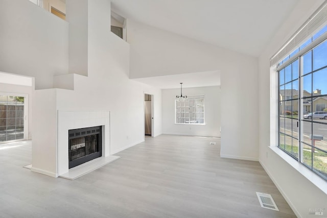 unfurnished living room featuring high vaulted ceiling, a wealth of natural light, wood finished floors, and visible vents