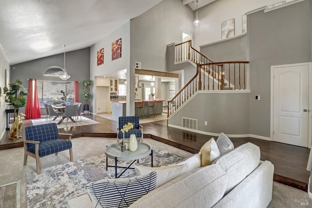 living room featuring high vaulted ceiling, baseboards, wood finished floors, visible vents, and stairway
