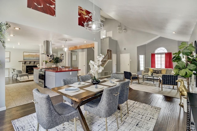 dining space with a fireplace, wood finished floors, stairway, high vaulted ceiling, and baseboards