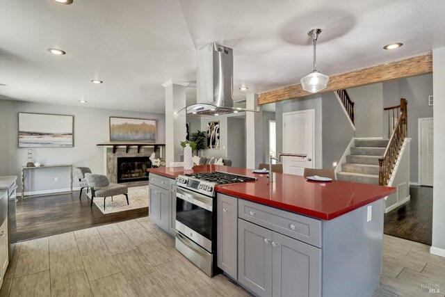 kitchen with island exhaust hood, a fireplace, gas stove, gray cabinetry, and open floor plan