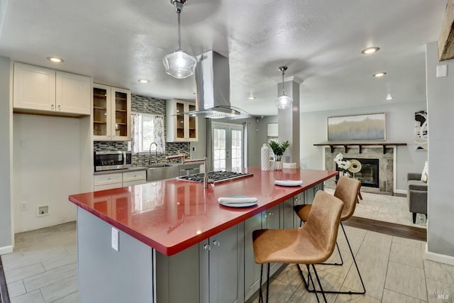 kitchen featuring appliances with stainless steel finishes, white cabinetry, island exhaust hood, a high end fireplace, and tasteful backsplash