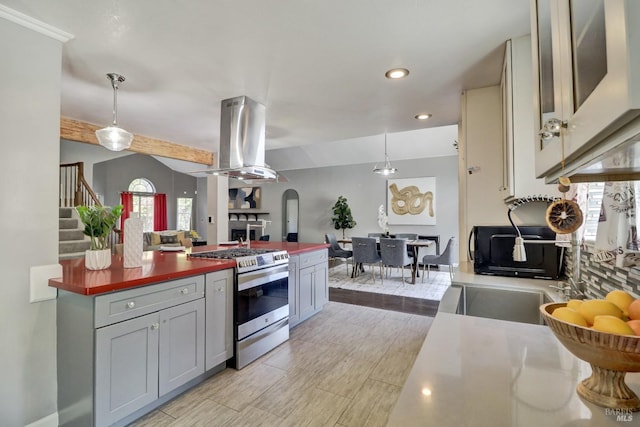 kitchen featuring stainless steel gas range oven, open floor plan, island exhaust hood, a healthy amount of sunlight, and gray cabinetry
