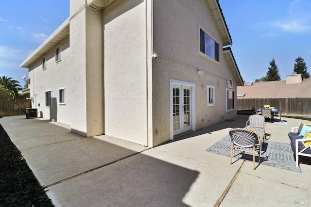 back of house featuring stucco siding, a fenced backyard, central AC unit, french doors, and a patio