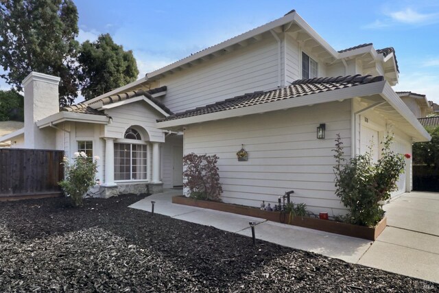 view of front of house featuring fence, a chimney, a tiled roof, and a garage