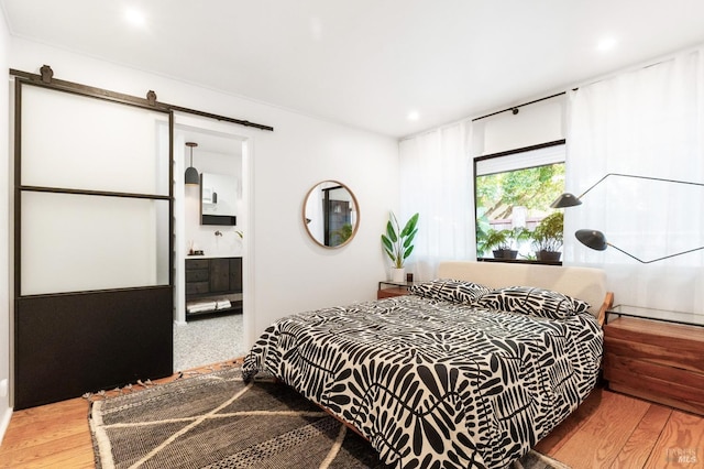 bedroom featuring recessed lighting, a barn door, connected bathroom, and wood finished floors