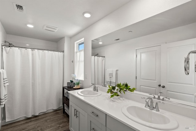 full bath with visible vents, a sink, wood finished floors, and double vanity