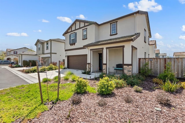 view of front facade with fence, stone siding, stucco siding, an attached garage, and driveway