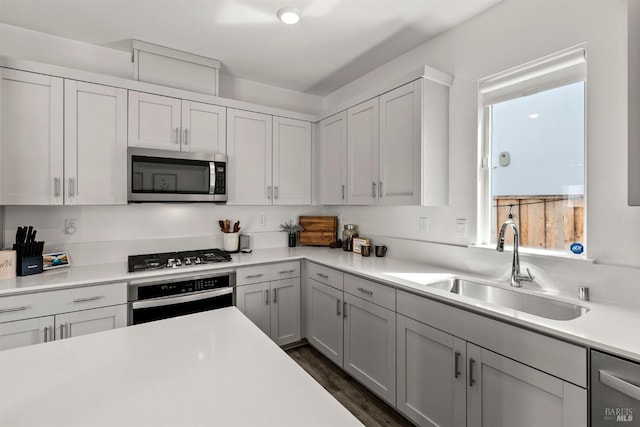 kitchen featuring appliances with stainless steel finishes, a sink, light countertops, dark wood finished floors, and white cabinetry
