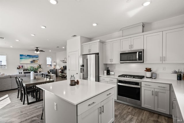 kitchen with wood finished floors, open floor plan, ceiling fan, light countertops, and stainless steel appliances