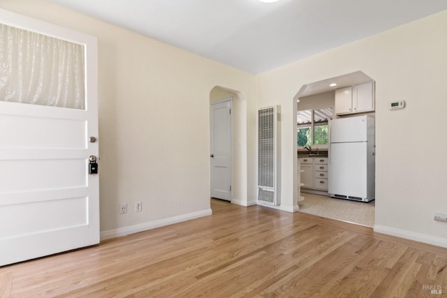 spare room with light wood-style floors, arched walkways, baseboards, and a heating unit
