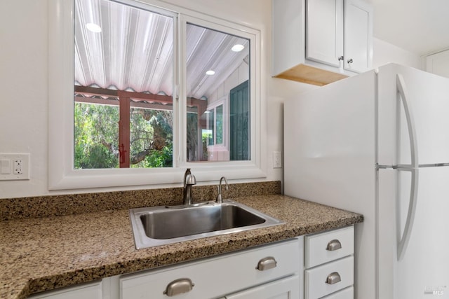 kitchen with freestanding refrigerator, a sink, white cabinets, and light stone countertops