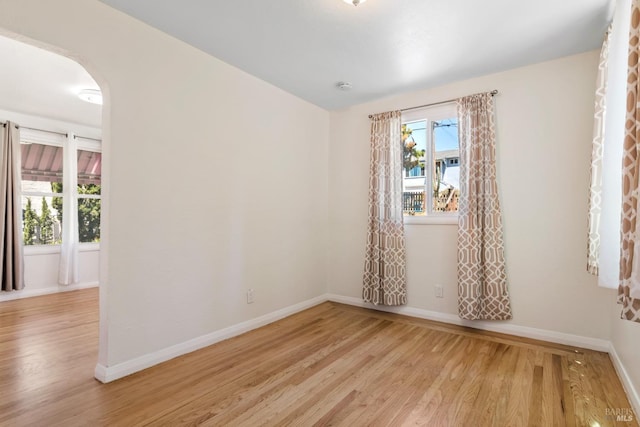 empty room featuring baseboards, arched walkways, and light wood-style flooring