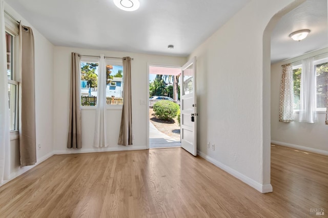 foyer entrance featuring light wood-type flooring, arched walkways, baseboards, and a wealth of natural light