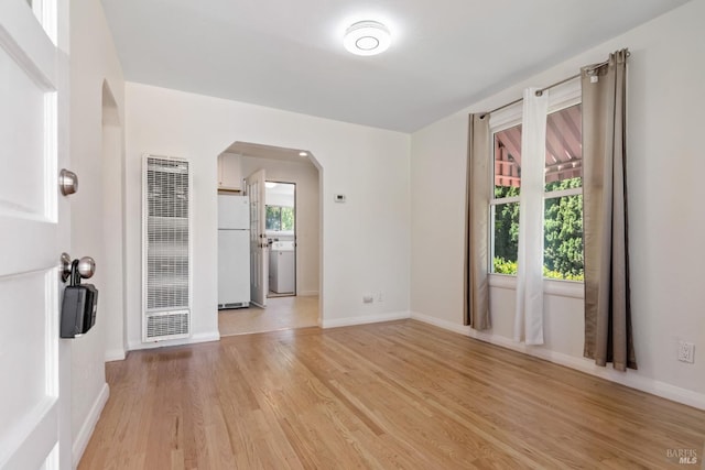 spare room with a heating unit, washer / dryer, baseboards, arched walkways, and light wood finished floors