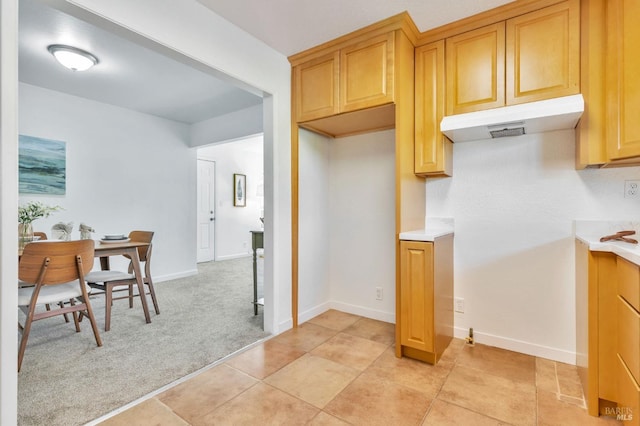 kitchen featuring light countertops, baseboards, light carpet, and under cabinet range hood