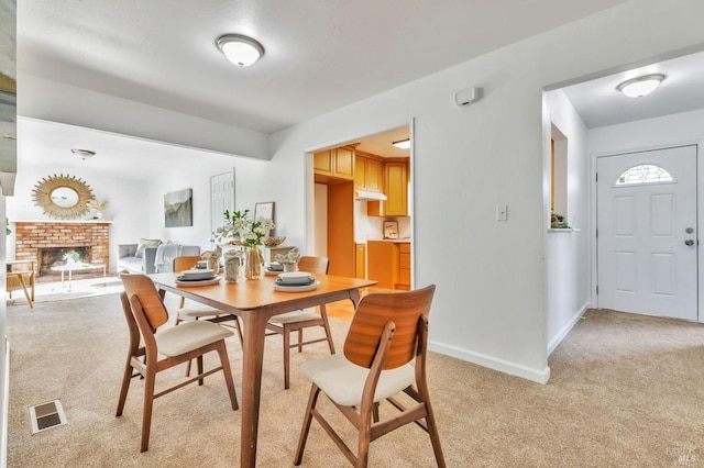 dining space with baseboards, light carpet, a brick fireplace, and visible vents