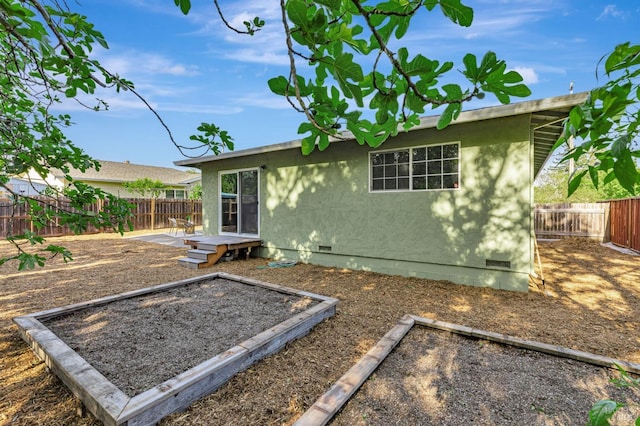 back of house with crawl space, a garden, and stucco siding