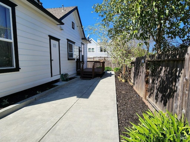 view of side of property featuring a fenced backyard, a patio, roof with shingles, and a wooden deck