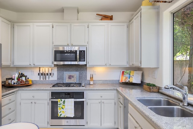 kitchen with a sink, appliances with stainless steel finishes, white cabinetry, and light countertops